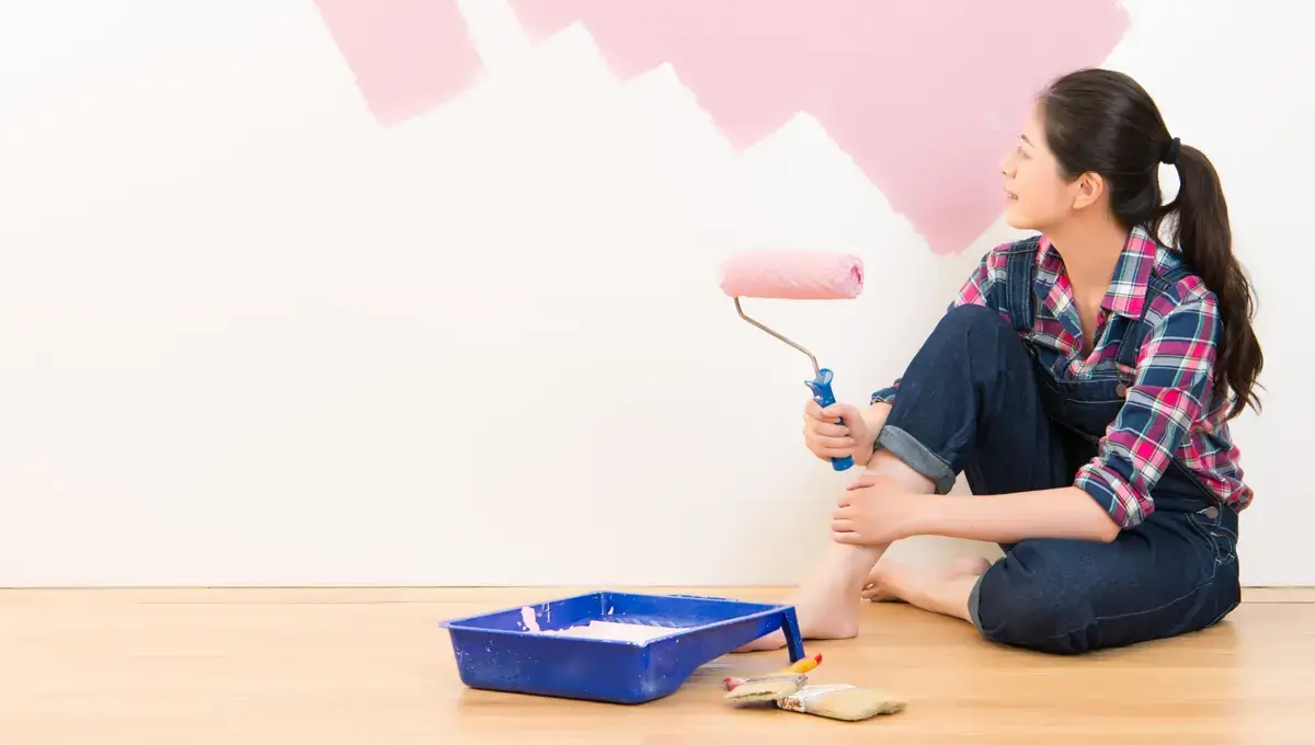 Eine Frau sitzt mit einer Malerwalze vor einer rosa bemalten Wand