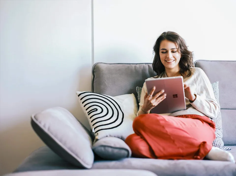 EIne Frau sitzt auf einem Sofa und schaut auf ihr Tablet