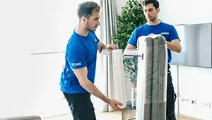 Umzug Wien: 2 Möbelpacker von DasUmzugsteam verpacken ein graues Sofa 